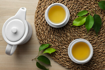 Green tea in white cups with leaves and teapot on wooden table, flat lay