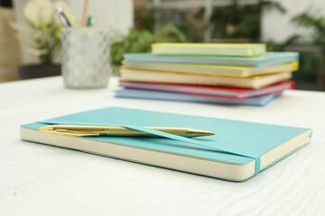 Turquoise planner and pen on white wooden table indoors, closeup