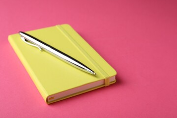 New stylish planner with hard cover and pen on pink background. Space for text