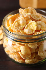 Jar of tasty crispy corn flakes on wooden table, closeup