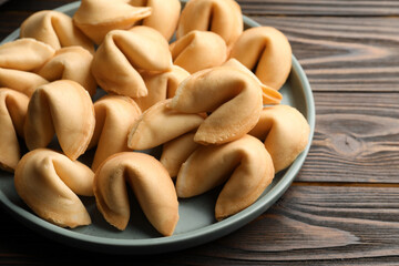 Tasty fortune cookies with predictions in plate on wooden table, closeup
