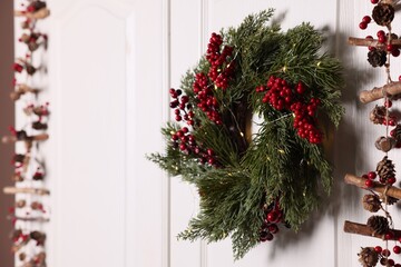 Beautiful Christmas wreath with red berries and fairy lights hanging on white door, space for text