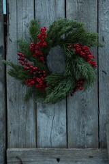 Fototapeta na wymiar Beautiful Christmas wreath with red berries hanging on wooden wall