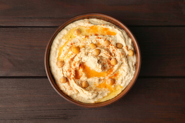 Bowl of tasty hummus with chickpeas and paprika on wooden table, top view