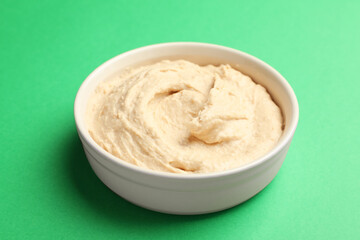 Bowl of tasty hummus on green background