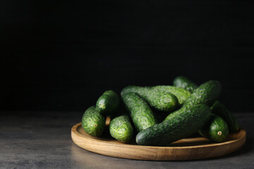 Wooden board with fresh ripe cucumbers on dark grey table, space for text