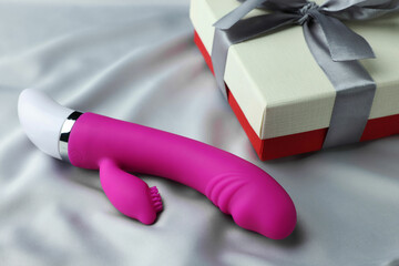 Gift box and pink vaginal vibrator on grey silk fabric. Sex toy - obrazy, fototapety, plakaty