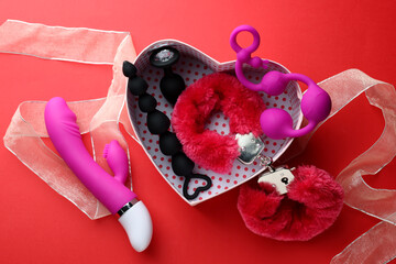 Gift box with different sex toys on red background, flat lay