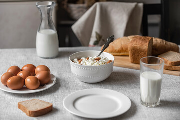 At home, in the kitchen, the table is covered with a linen tablecloth and there are natural and healthy products, milk and cottage cheese, bread and boiled chicken eggs on it