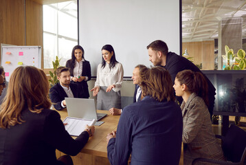 Business colleagues discuss development strategy and financial results in office at briefing. Business woman points to laptop and talks to people sitting at table in office with loft interior