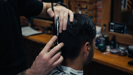 Barber holding comb and cutting hair of man in blurred barbershop.