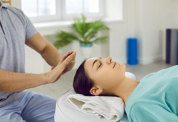 Beautiful young woman relaxing and restoring energy during Reiki therapy session with Reiki healer. Holistic treatment, Reiki healing, spiritual therapy, regaining harmony concepts