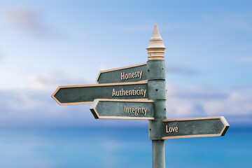 honesty authenticity integrity love four word quote written on fancy steel signpost outdoors by the sea. Soft Blue ocean bokeh background.