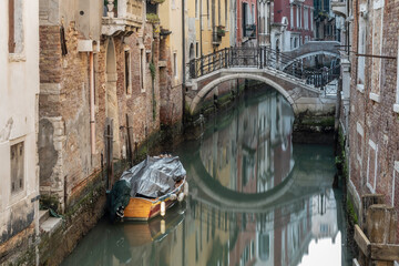 Typical Venetian canal, early in the morning. Venice, Italy. The buildings are reflecting on the calm water