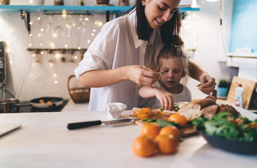 Cheerful mother and daughter preparing breakfast at kitchen
