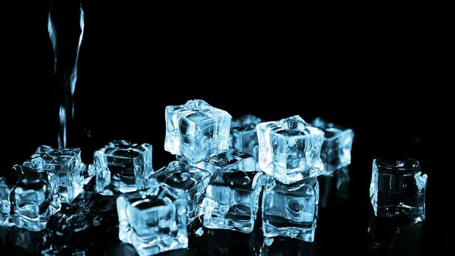 A stream of water falls on ice cubes on a black background. Slow motion.