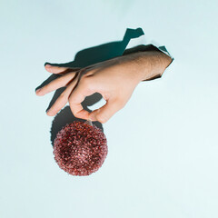 A man's hand holds a shiny Christmas decorative ball, creative  layout against pastel blue...