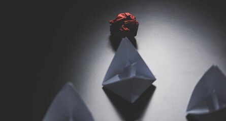 Several paper boats are on the table. one of them is red concept of leadership.
