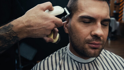 Tattooed barber trimming hair of man in barbershop.