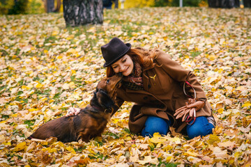 Young red-haired woman walking in the park with a red dachshund dog. The dog reaches out to the owner 