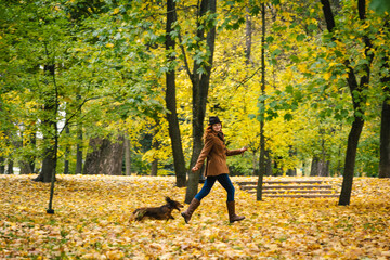 Young red-haired woman running in the park with a red dachshund dog. 