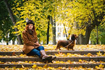 Young red-haired woman posing in the park with a red dachshund dog. 