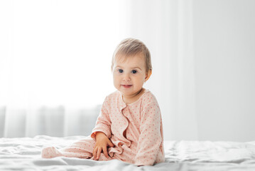 Fototapeta premium Little baby girl in pink pajamas on the bed