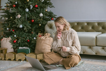 Attractive woman shopping online at holiday sales at home. Using laptop. Christmas shopping. Home interior.