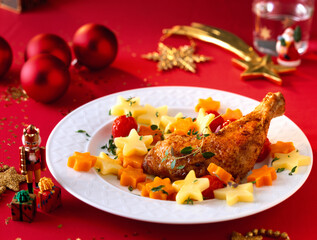 Chicken leg with star shaped carrots and potatoes on a white plate on a Christmassy decorated table