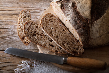 Traditional bread on cutting board. Sliced wholemeal loaf and knife on old wooden table, closeup.