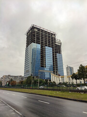 Fototapeta na wymiar A huge unfinished skyscraper with glass walls on the background of an asphalt road