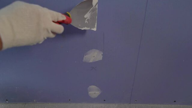 Applying putty to the gypsum plasterboards. Plastering wall with putty-knife, close up image. Fixing wall surface and preparation for painting.