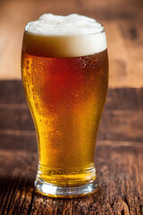 closeup of beer with foam in glass laying on rustic wooden table
