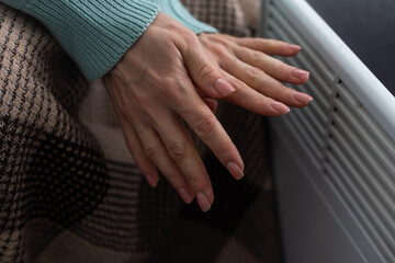Woman warming hands near heater indoors, closeup