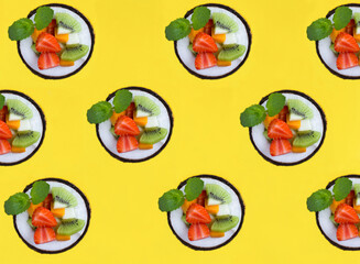 Fruit salad in the half coconut on the yellow background. Flat lay. Pattern.