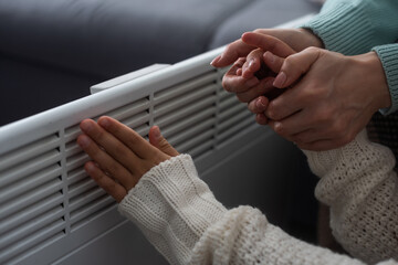 At the electric heater, people are warming themselves, covered with a warm blanket at home. hands...