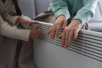 Mother and child warming hands near electric heater at home, closeup.