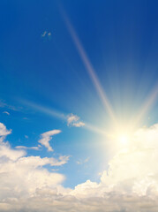 Blue summer sky with fluffy clouds and bright sun as a background. Vertical photo.