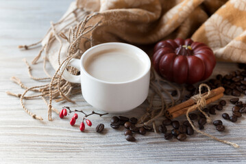 Obraz na płótnie Canvas Cozy composition. Cup of coffee with cream, pumpkin candle, coffee beans, cinnamon sticks and fabric scarf on the light wooden background. Top view