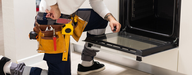 Professional serviceman repairing modern oven in kitchen