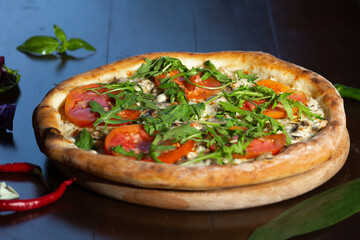 Tasty pizza and cooking ingredients tomatoes basil on black concrete background. Top view of hot pepperoni pizza. 