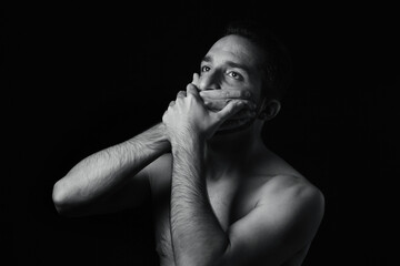 The man covers his mouth with his hands. Black-white portrait of a man on a black background.