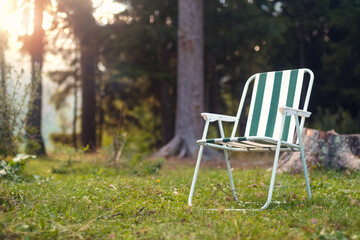 Empty folding camp chair for relaxing on the field near the forest with blurred sunset background