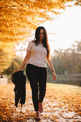 Young woman walking in park under trees with orange leaves during sunny weather in autumn
