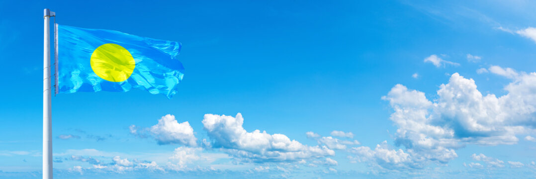 Palau flag waving on a blue sky in beautiful clouds - Horizontal banner