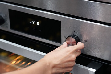 Woman's hand adjusting electric oven in kitchen, closeup                            