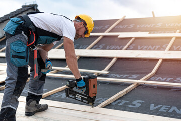 Carpenter working on the roof. Nailing wooden boards using an automatic nailer.