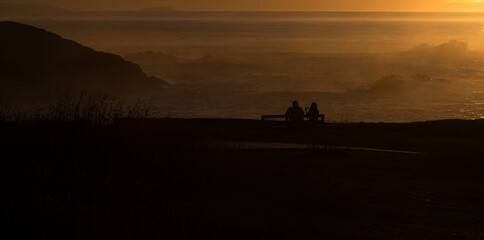 Fototapeta na wymiar Silhouettes of two people sitting on a bench near the ocean at sunset