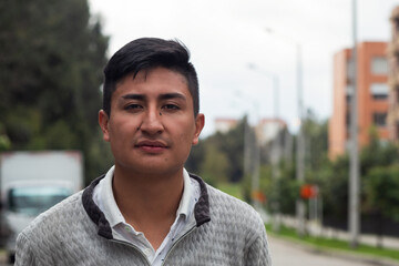 Close up on the face of a serious young Latin man looking at the camera on a street during a gray day