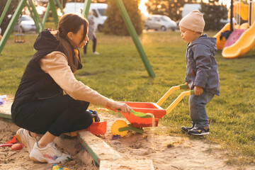 Mother and child playing with wheelbarrow in sandbox. Little builder. Education, and imagination, purposefulness concept. Support childhood parenthood symbol